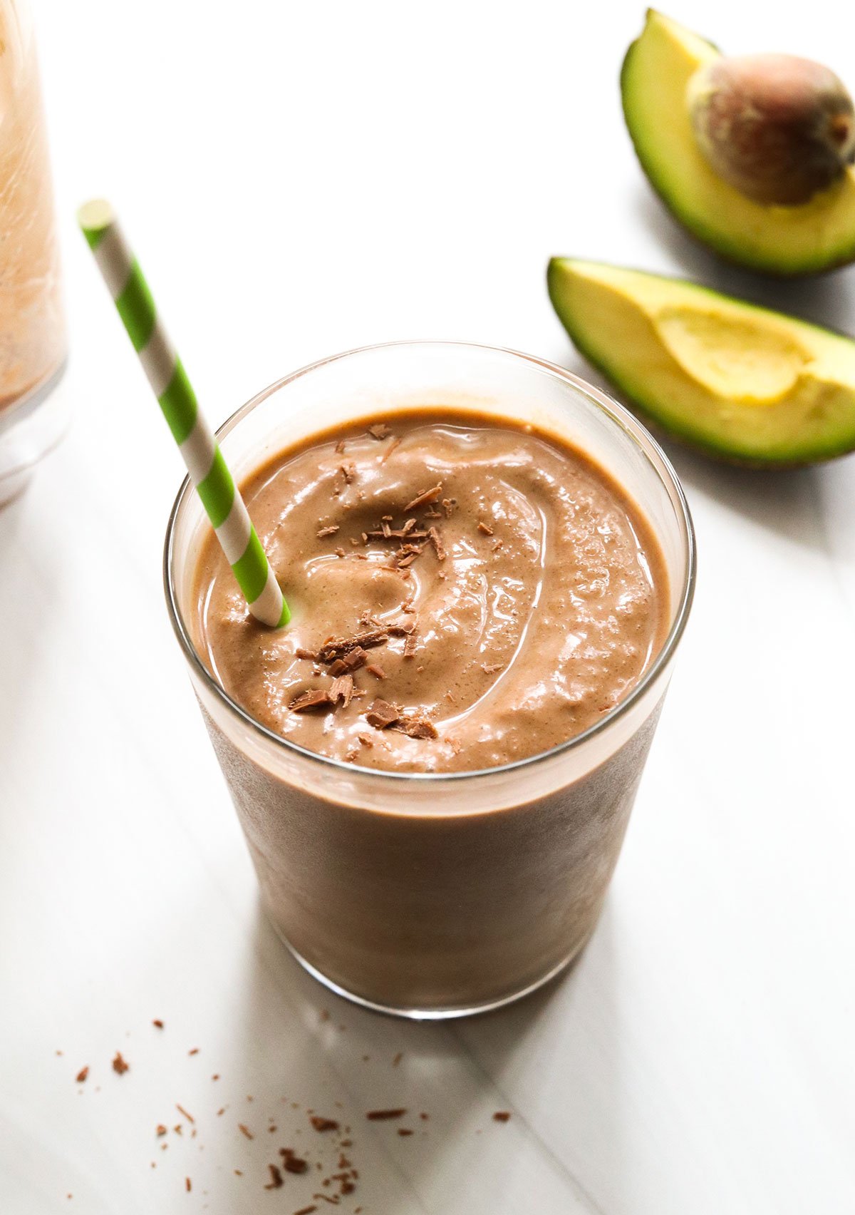 chocolate avocado smoothie with straw and avocado in background.