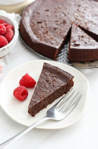 flourless chocolate cake slice on plate with raspberries.
