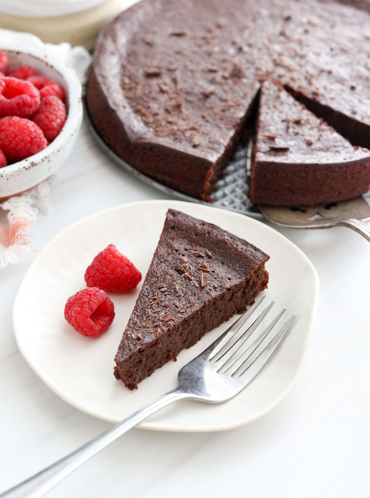 flourless chocolate cake slice on plate with raspberries.