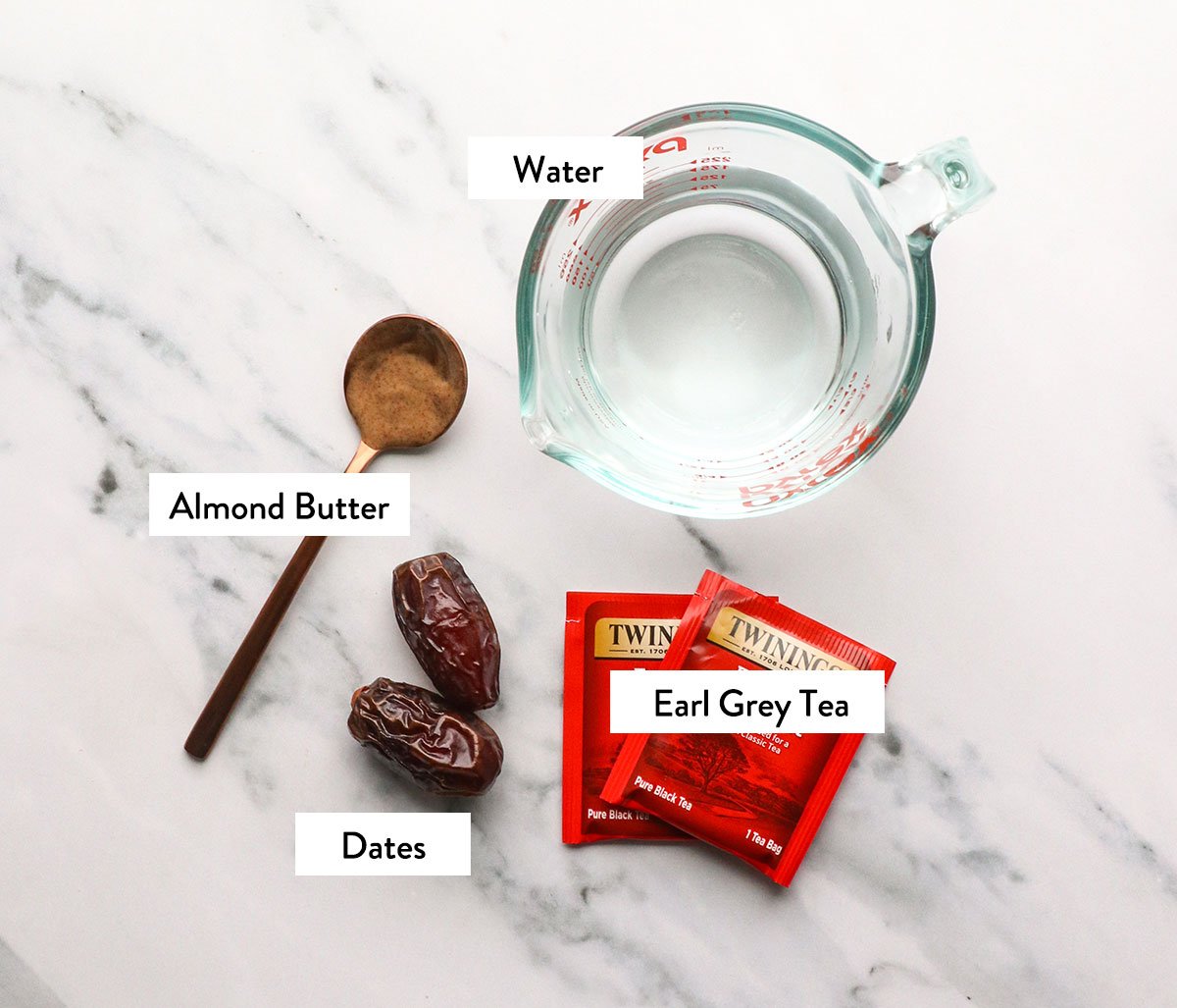 tea bags, dates, almond butter and water labeled on a white surface. 