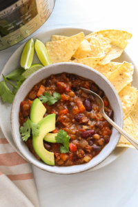 instant pot vegan chili served in a bowl with tortilla chips and sliced avocado.
