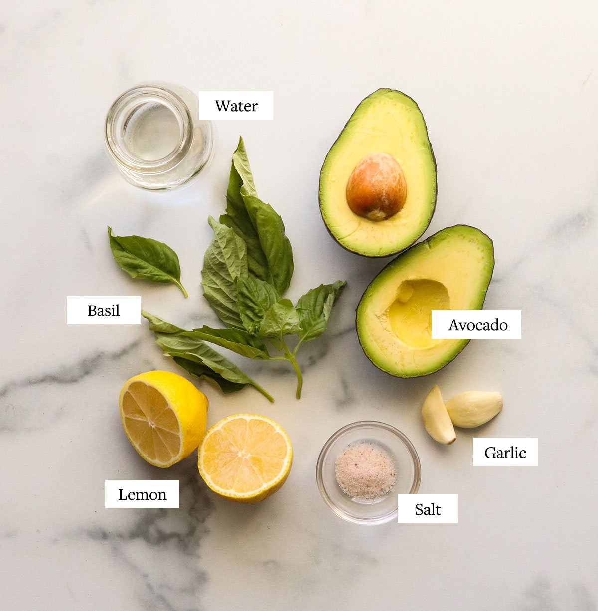 avocado pesto ingredients labeled on a marble surface.