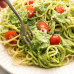 avocado pesto sauce twirled on a fork with pasta and cherry tomatoes.