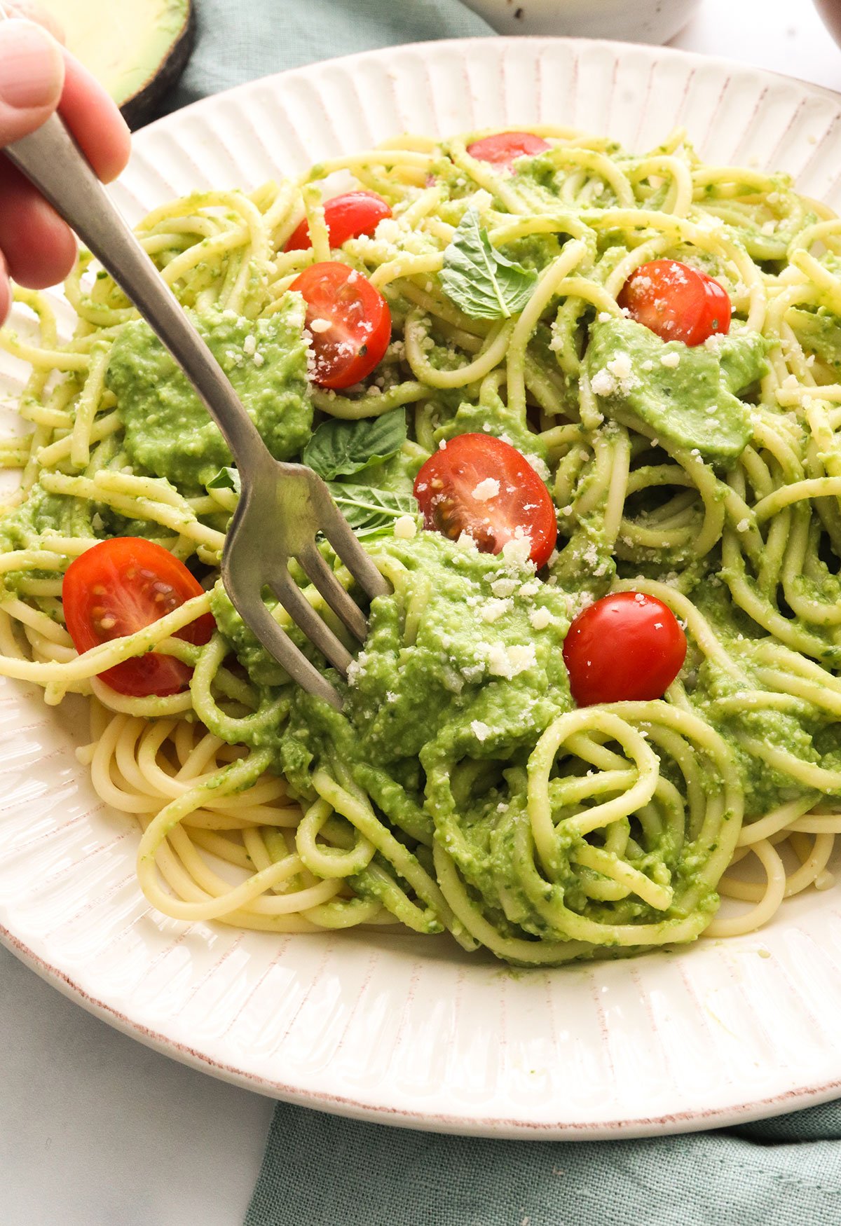 avocado pesto sauce twirled on a fork with pasta and cherry tomatoes.