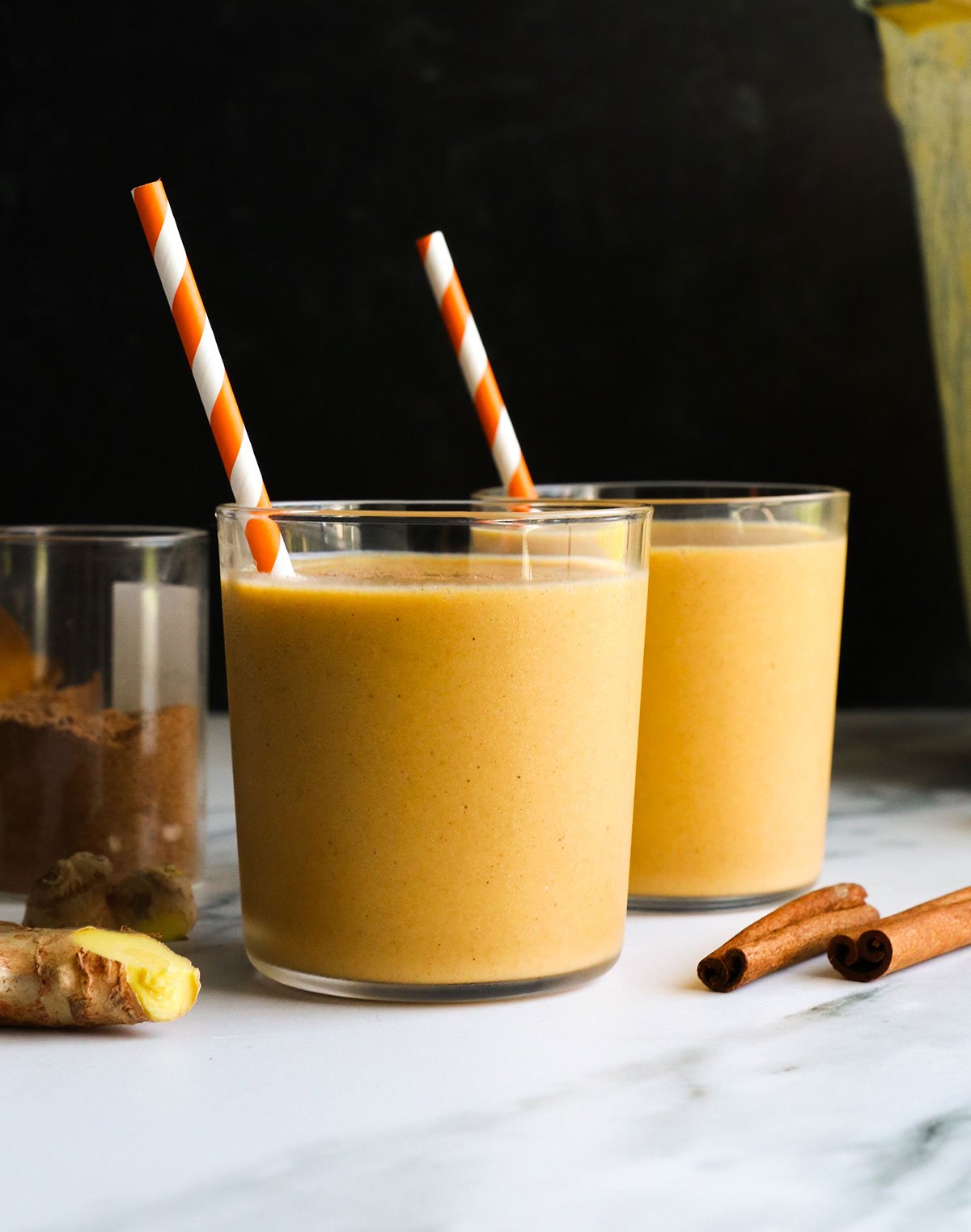 sweet potato smoothie in two small glasses with a black background. 