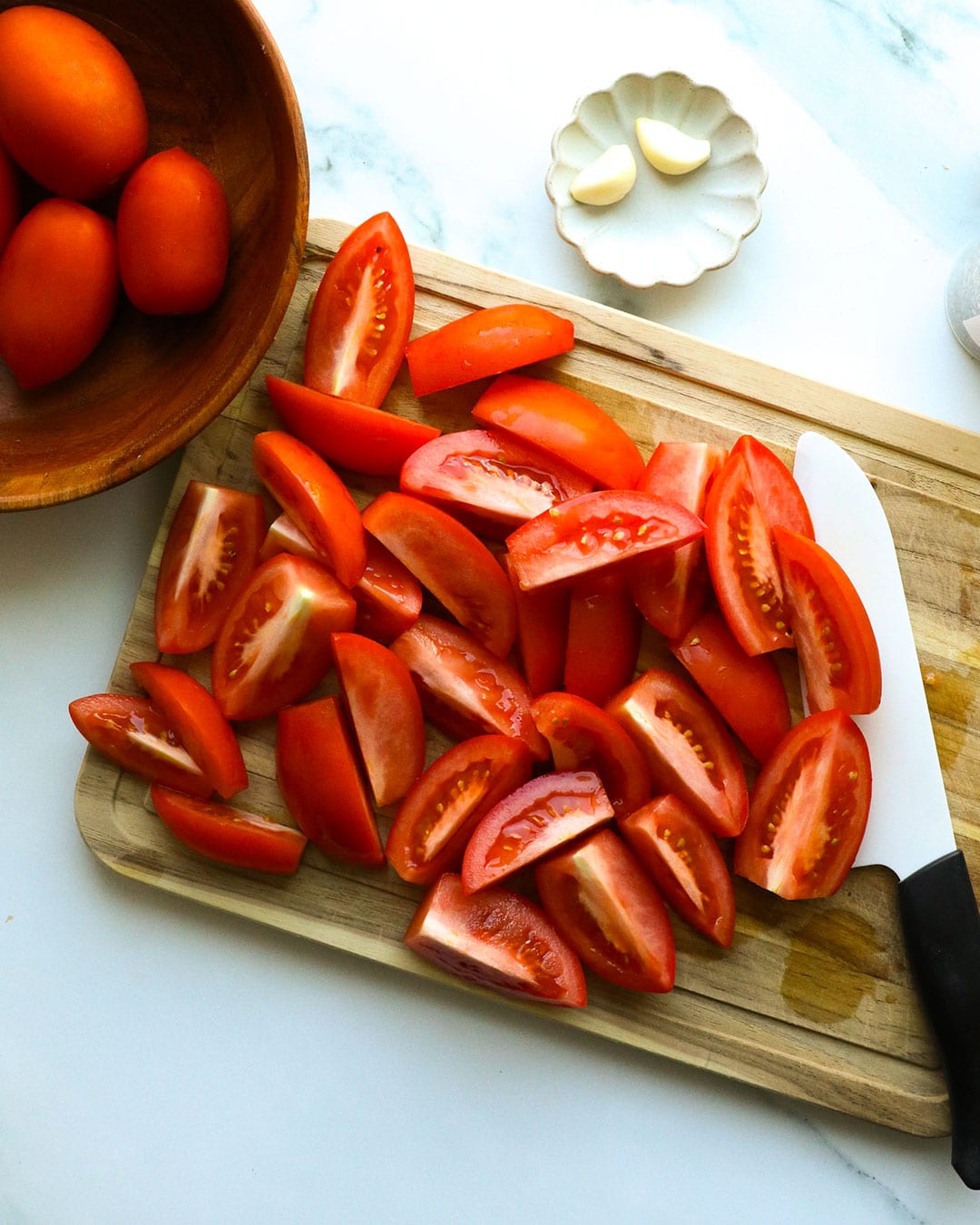 tomatoes quartered on a cutting board. 