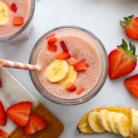 strawberry banana smoothie divided into two glasses and topped with fruit.