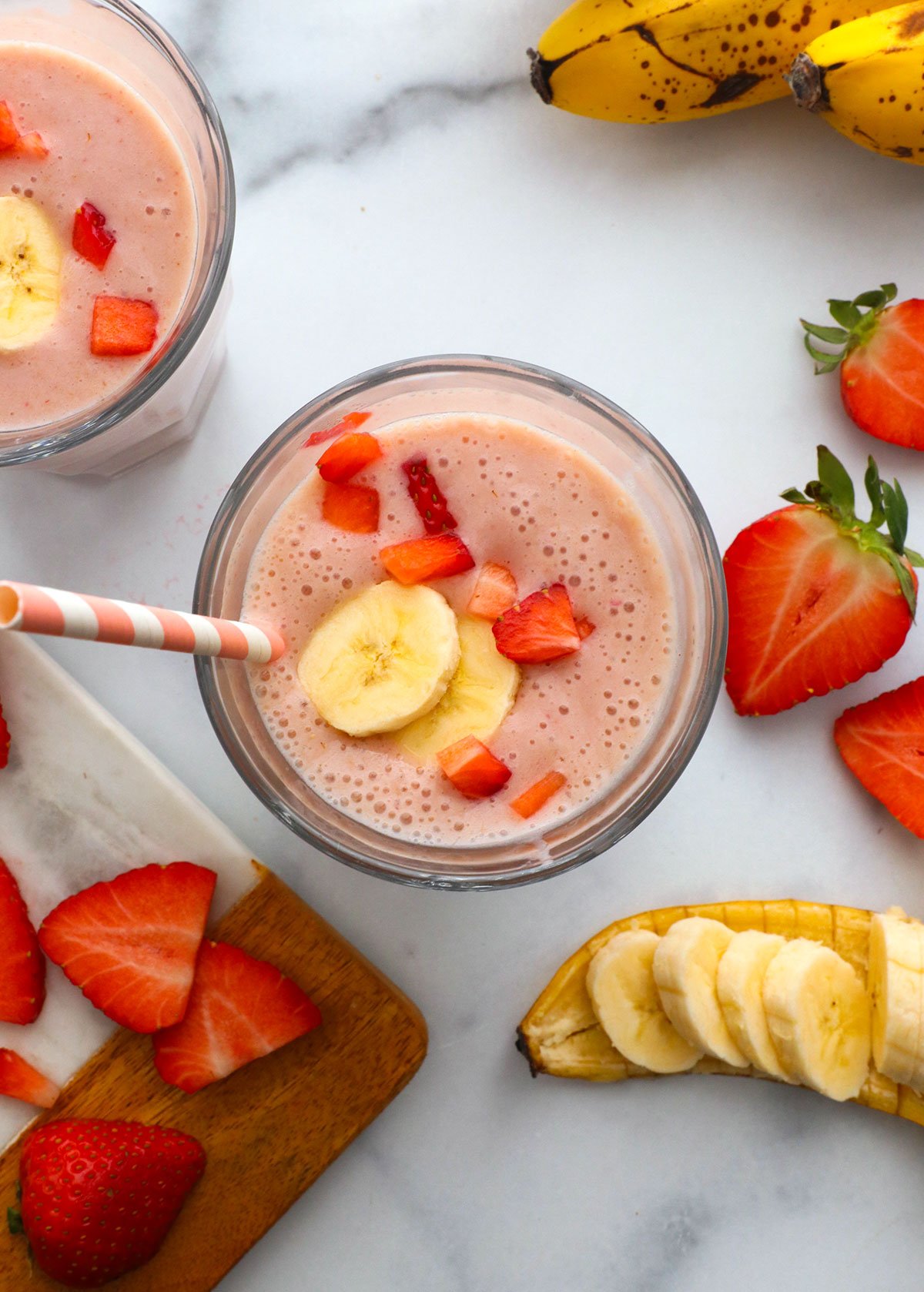 strawberry banana smoothie divided into two glasses and topped with fruit.