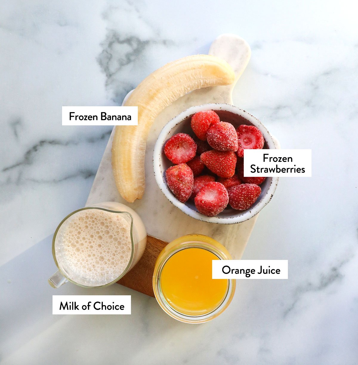 frozen banana, strawberries, milk and OJ labeled on a marble surface.