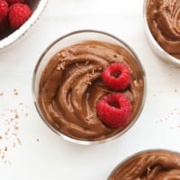 chocolate avocado pudding topped with raspberries and chocolate shavings.