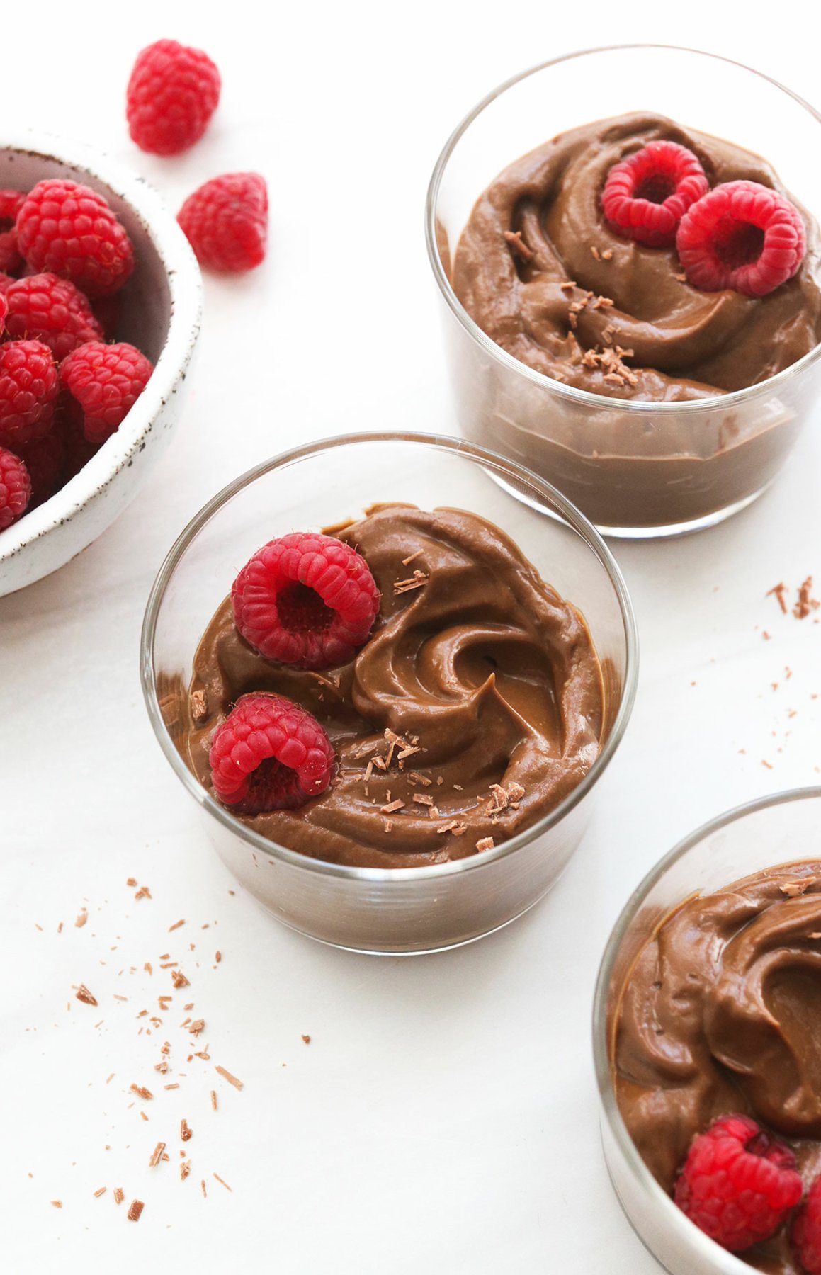 3 glass bowls of chocolate avocado pudding topped with fresh raspberries.