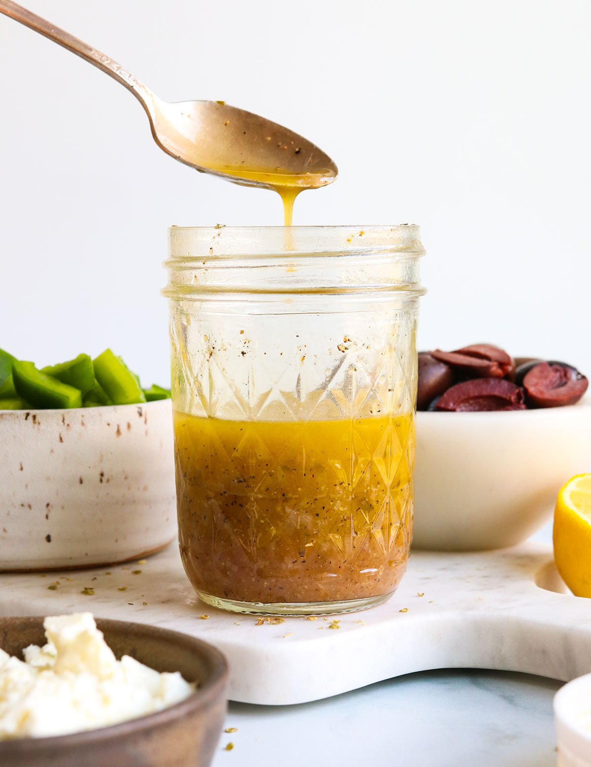Greek dressing poured off of a spoon into a glass jar.