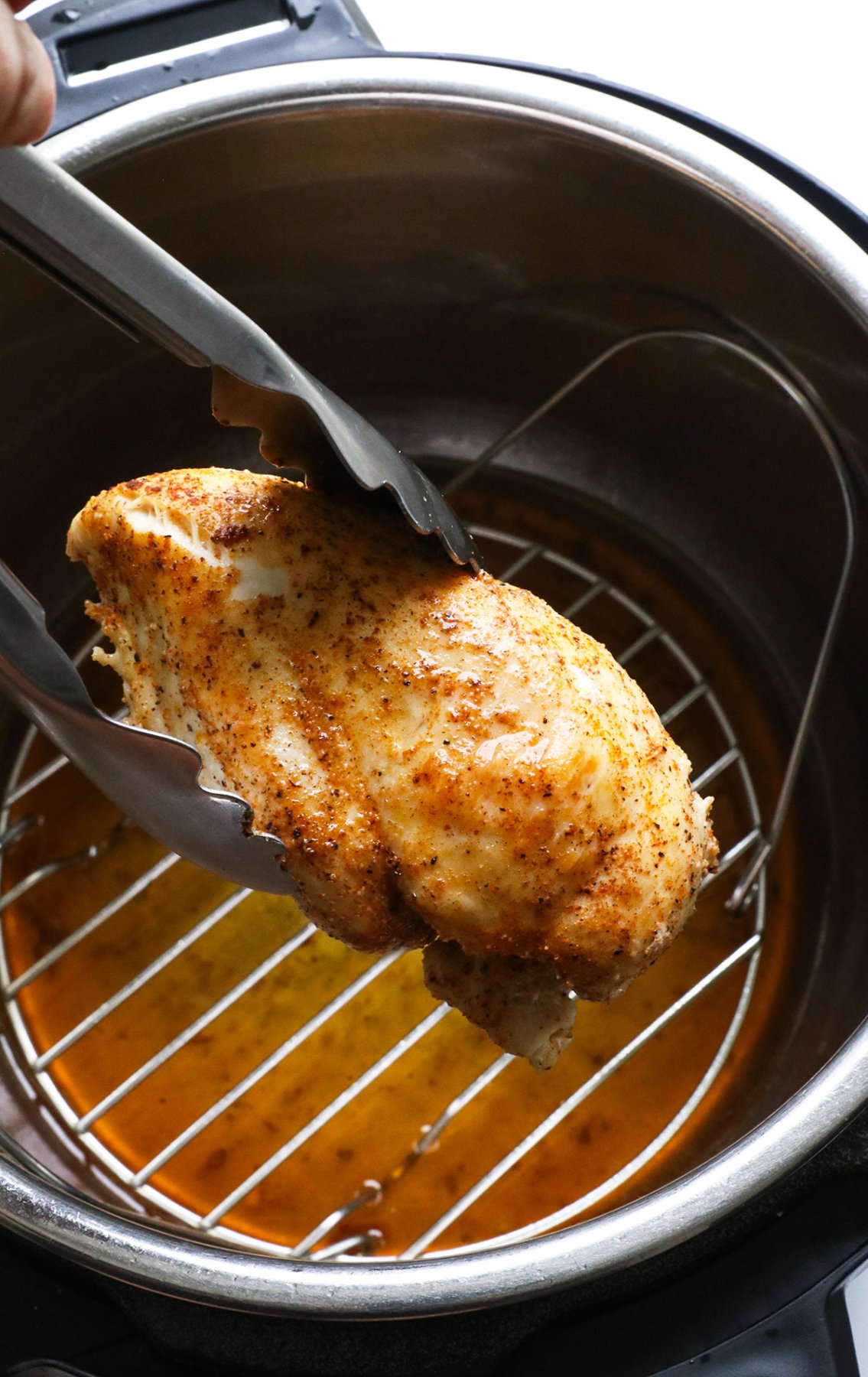 Juicy instant pot chicken breast lifted up with tongs.