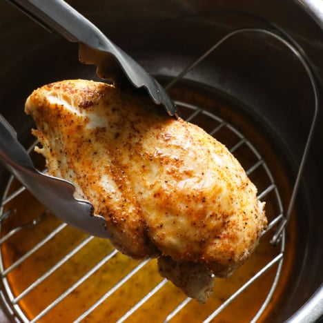 Juicy instant pot chicken breast lifted up with tongs.