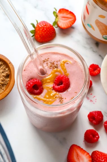 peanut butter jelly smoothie in a glass with raspberries on top.