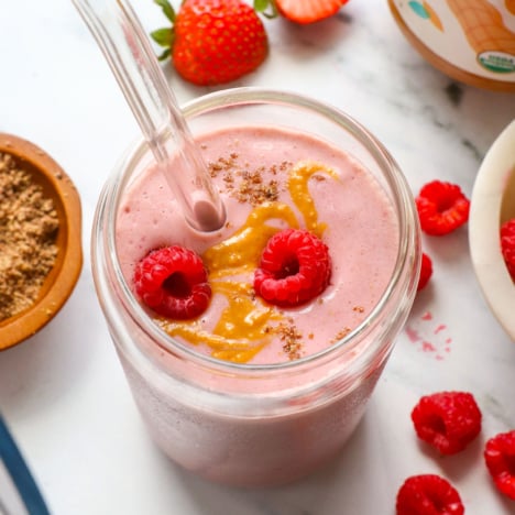 peanut butter jelly smoothie in a glass with raspberries on top.