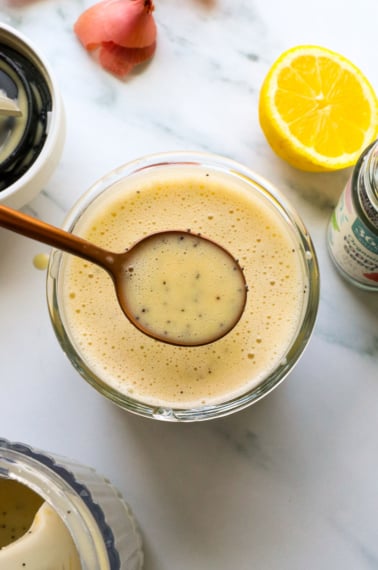 poppy seed dressing lifted on a spoon from a glass jar.