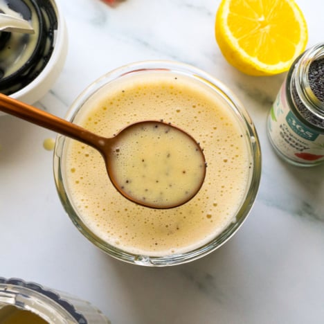 poppy seed dressing lifted on a spoon from a glass jar.
