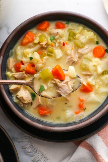 leftover turkey soup lifted on a spoon over a bowl.