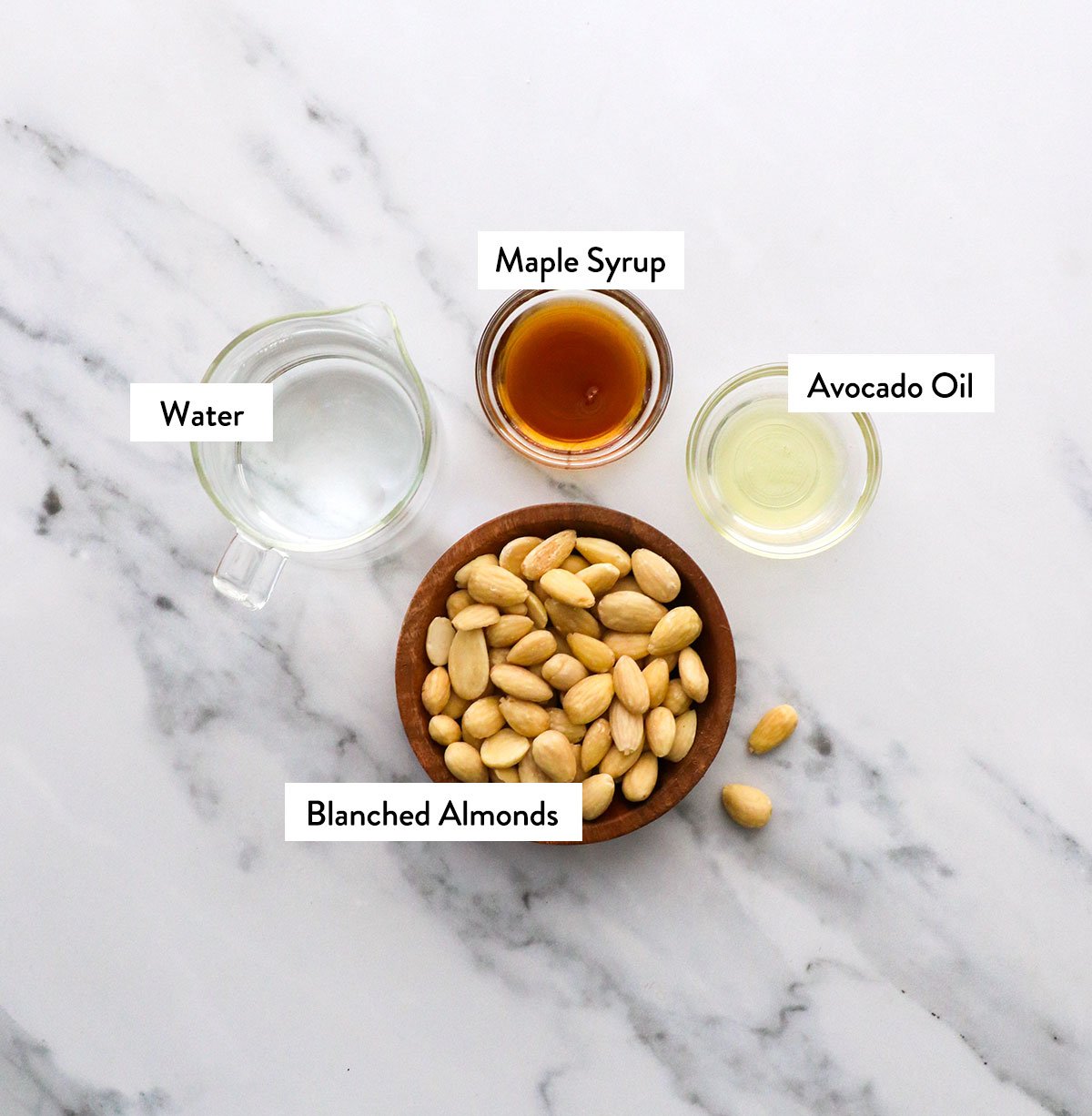 blanched almonds, maple syrup, water, and avocado oil labeled in bowls.