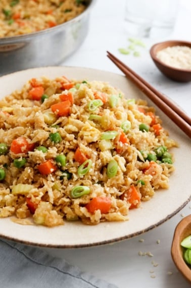 cauiflower fried rice served on plate with chopsticks.