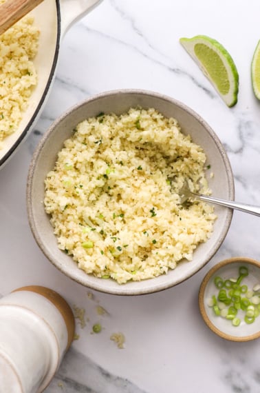 cooked cauliflower rice in a bowl with green onion.