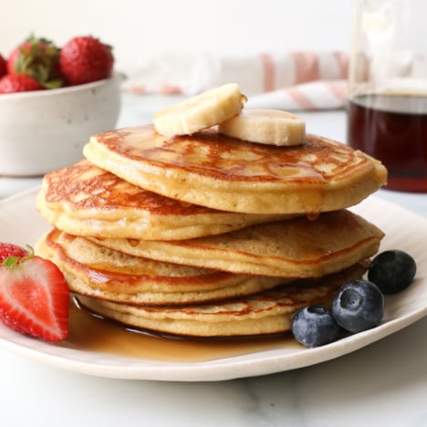 coconut flour pancakes stacked on a plate with fruit.