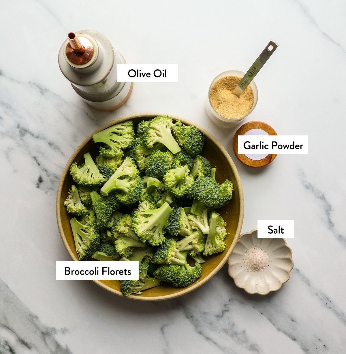 broccoli, olive oil, garlic powder, and salt labeled on a white surface. 