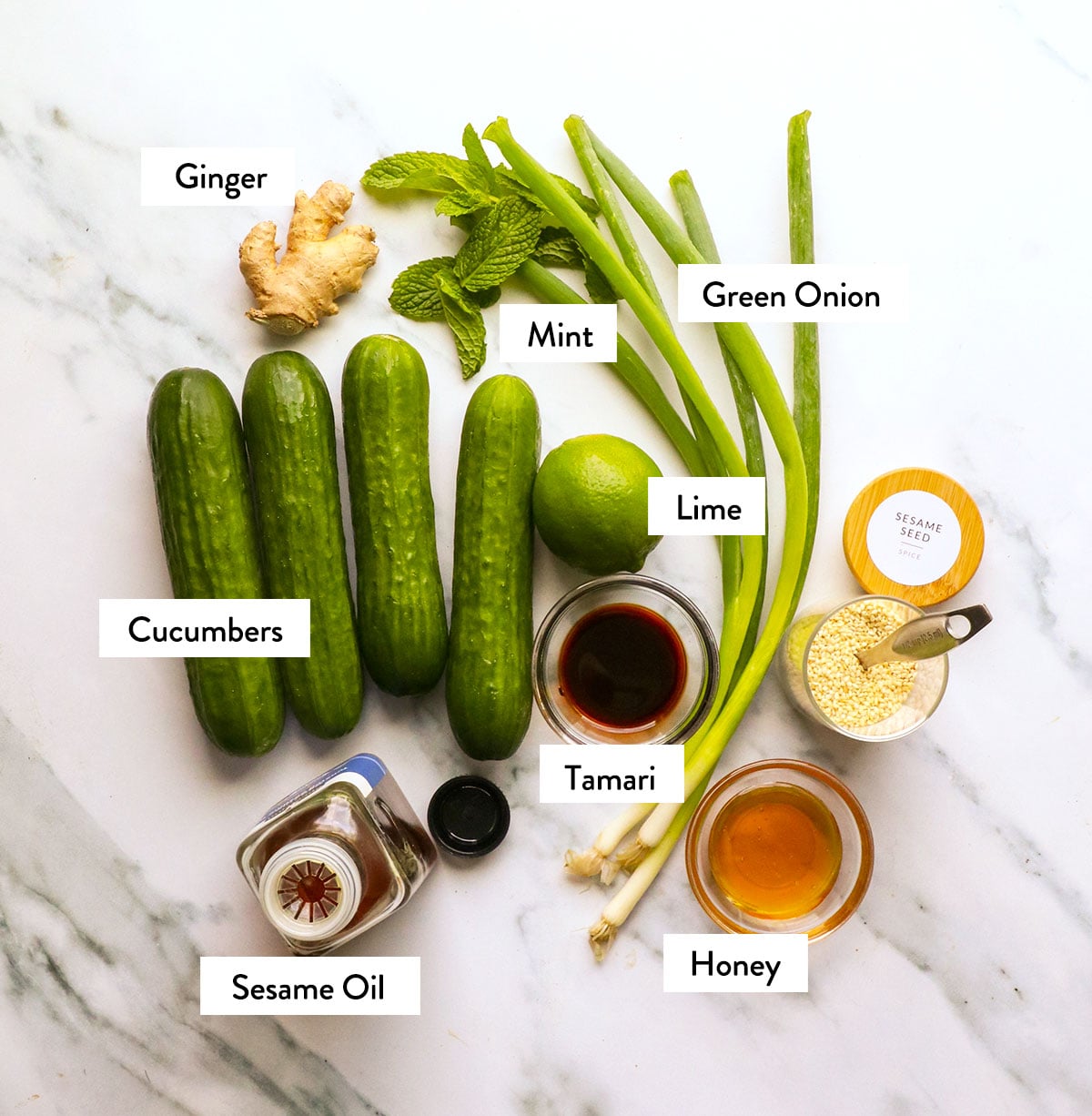 cucumbers, green onion, mint, sesame oil, and honey labeled on a white surface. 