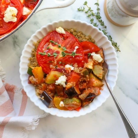 White bowl filled with quinoa and cooked ratatouille with a fork.