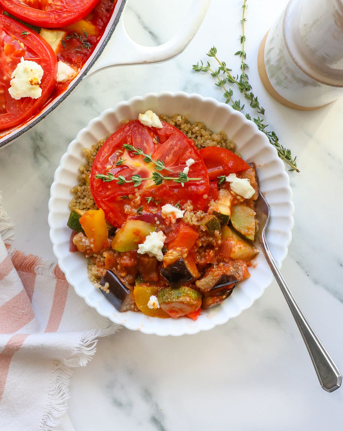 White bowl filled with quinoa and cooked ratatouille with a fork.
