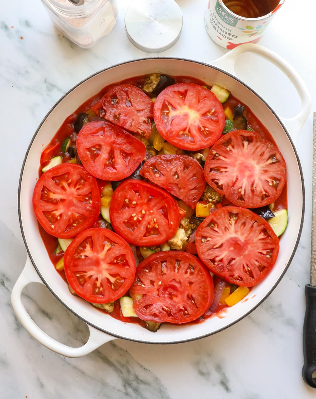 zucchini and sliced tomatoes added to the white pan full of sauce.