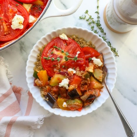 ratatouille served over quinoa in a white bowl with fresh thyme on top.