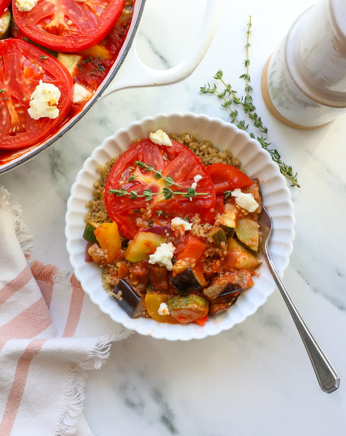 ratatouille served over quinoa in a white bowl with fresh thyme on top.