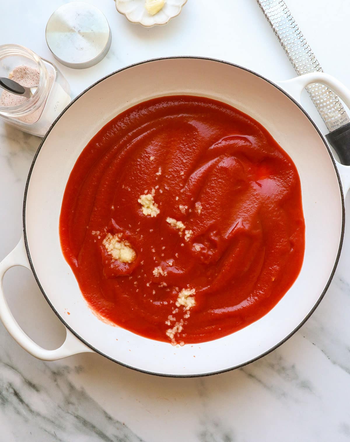 tomato sauce added to a large white pan with garlic inside.