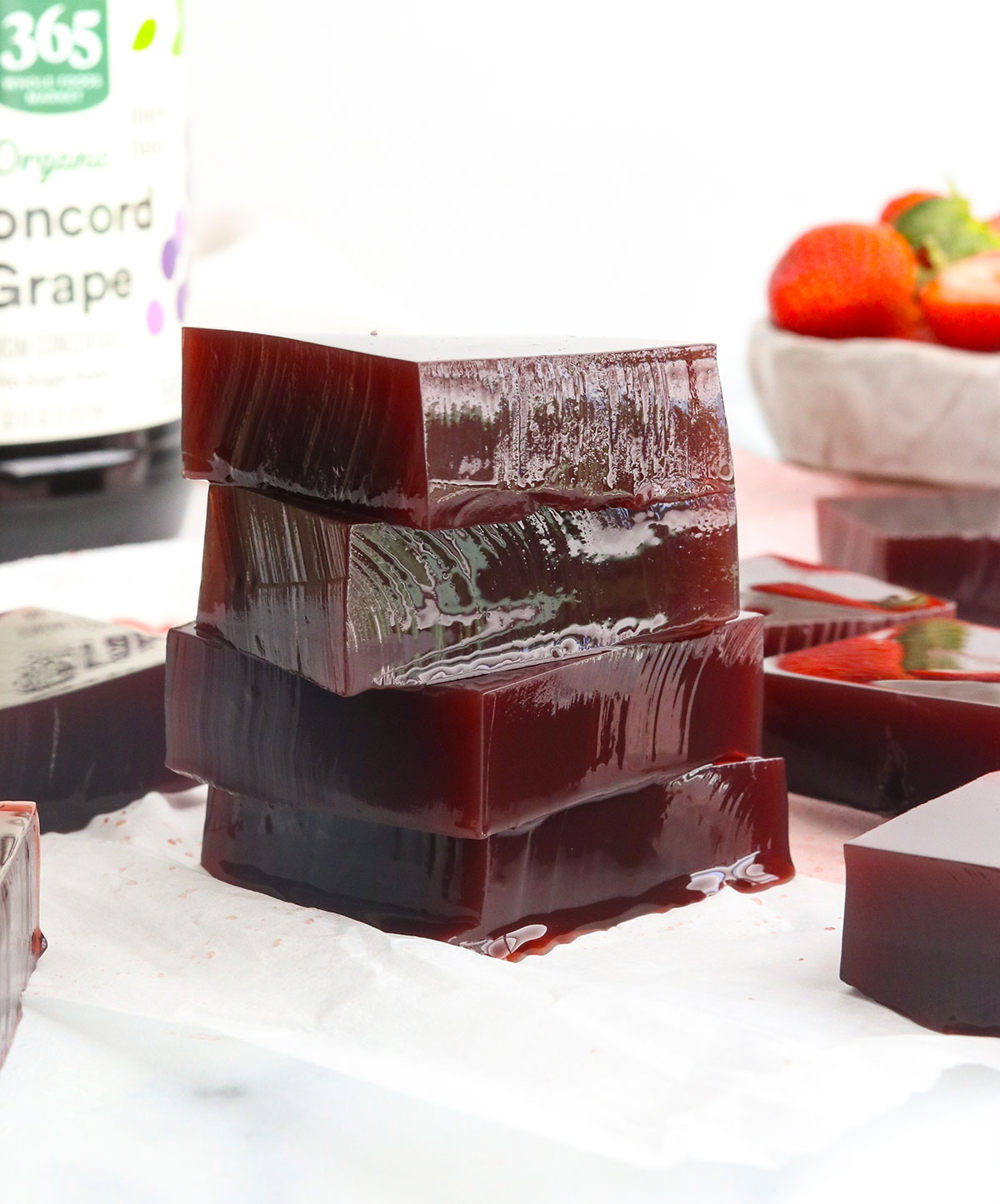 4 squares of vegan jello stacked in front of a grape juice container.