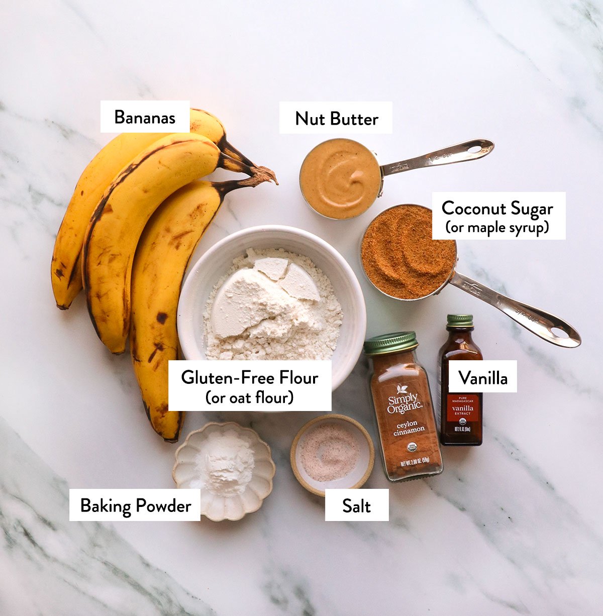 bananas, gluten-free flour, coconut sugar, nut butter, and spices labeled on a white surface.