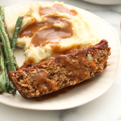 vegan meatloaf slice on a plate with mashed potatoes, green beans, and gravy.