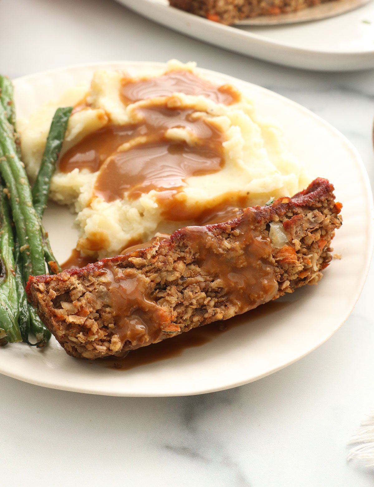 vegan meatloaf slice on a plate with mashed potatoes, green beans, and gravy. 