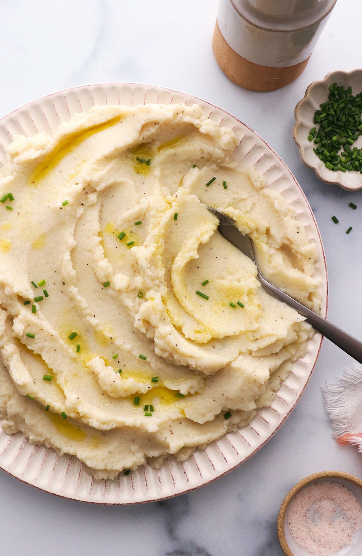 mashed cauliflower topped with chives and served with a spoon.