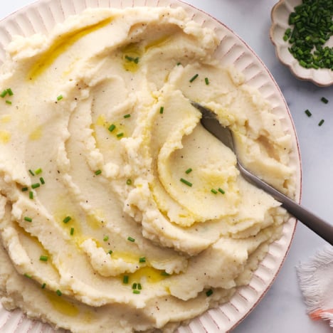 mashed cauliflower topped with chives and served with a spoon.