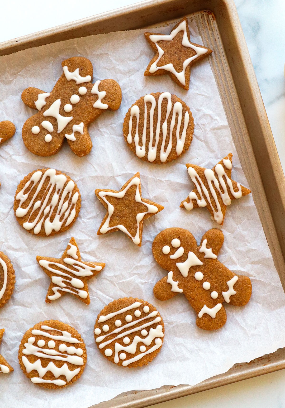 almond flour gingerbread cookies decorated with frosting on a parchment lined pan.