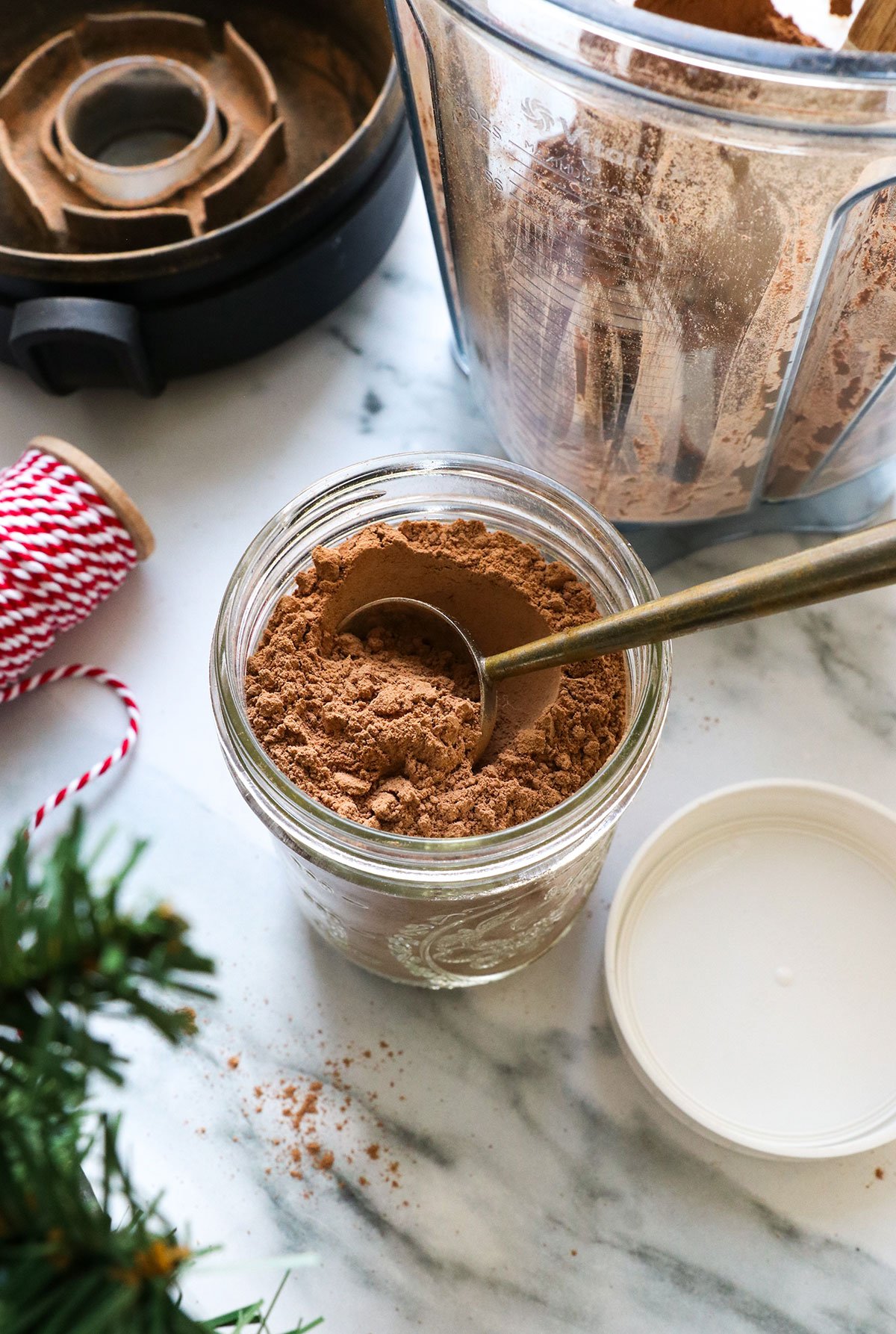 hot chocolate mix with a tablespoon in a glass jar with ribbon nearby.