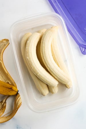 Frozen bananas stored whole in a plastic container.