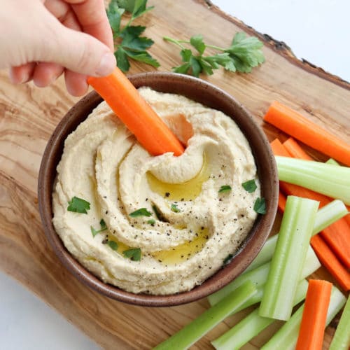 hand dipping carrot into hummus