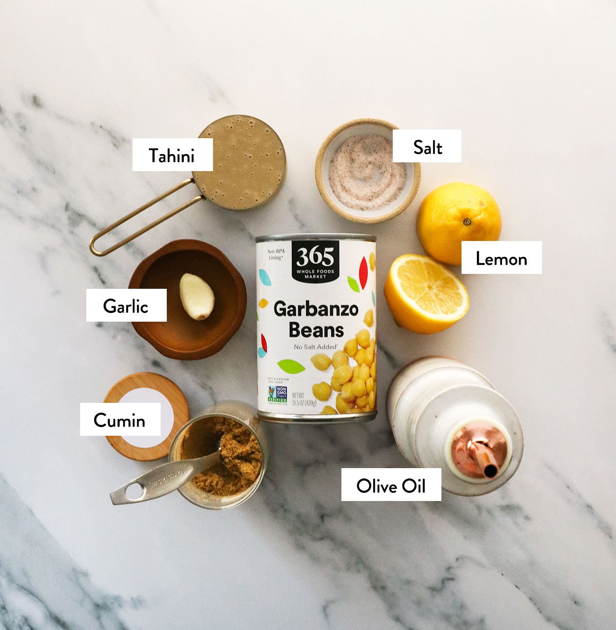 canned chickpeas, tahini, lemon, olive oil, garlic, and spices labeled in bowls.