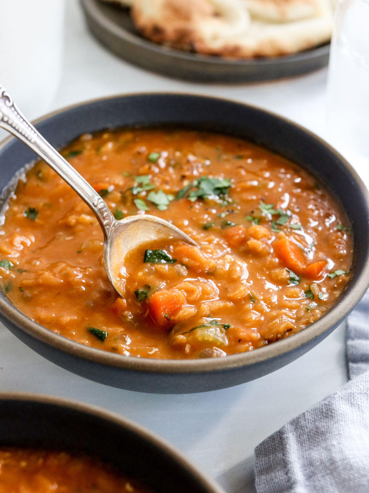 cucchiaio sollevando la zuppa di lenticchie rosse da una ciotola nera.