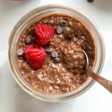close up of chocolate chia pudding in a jar with fresh raspberries and chocolate chips.