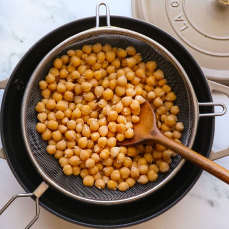 cooked chickpeas from scratch in a strainer over a black pot.