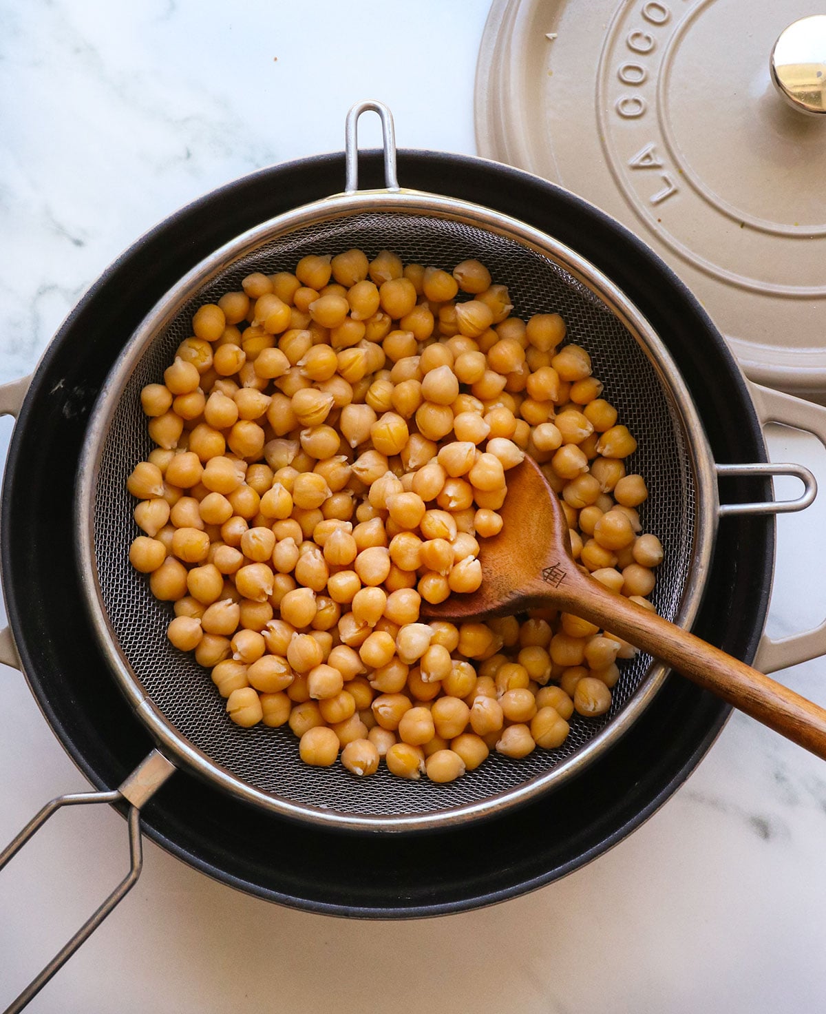 cooked chickpeas from scratch in a strainer over a black pot.